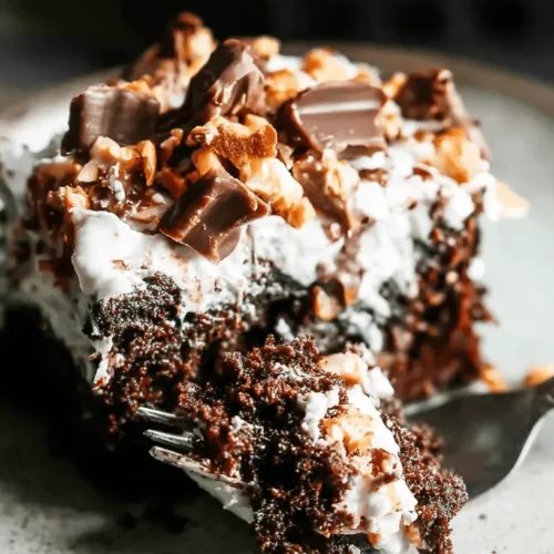 A decadent slice of Better Than Sex Cake with rich chocolate, fluffy white topping, chocolate chunks, and nuts, being lifted by a fork on a rustic plate.