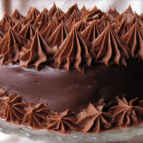 A decadent extreme chocolate cake with dark frosting and intricate piped swirls, presented on a glass stand.