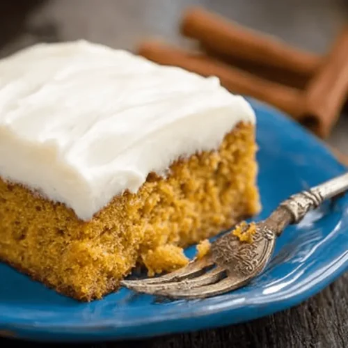 Delicious slice of pumpkin cake with creamy white frosting on a vibrant blue plate.