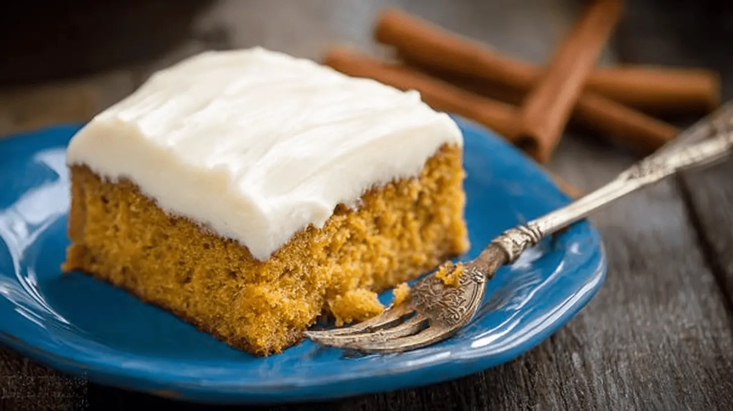 Delicious slice of pumpkin cake with creamy white frosting on a vibrant blue plate.