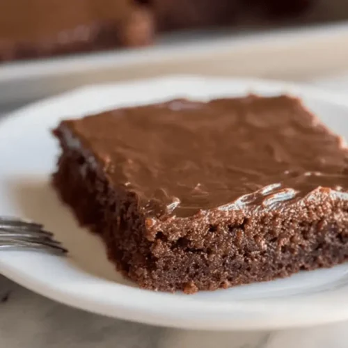 Delicious slice of chocolate Texas sheet cake with fudge frosting on a white plate.