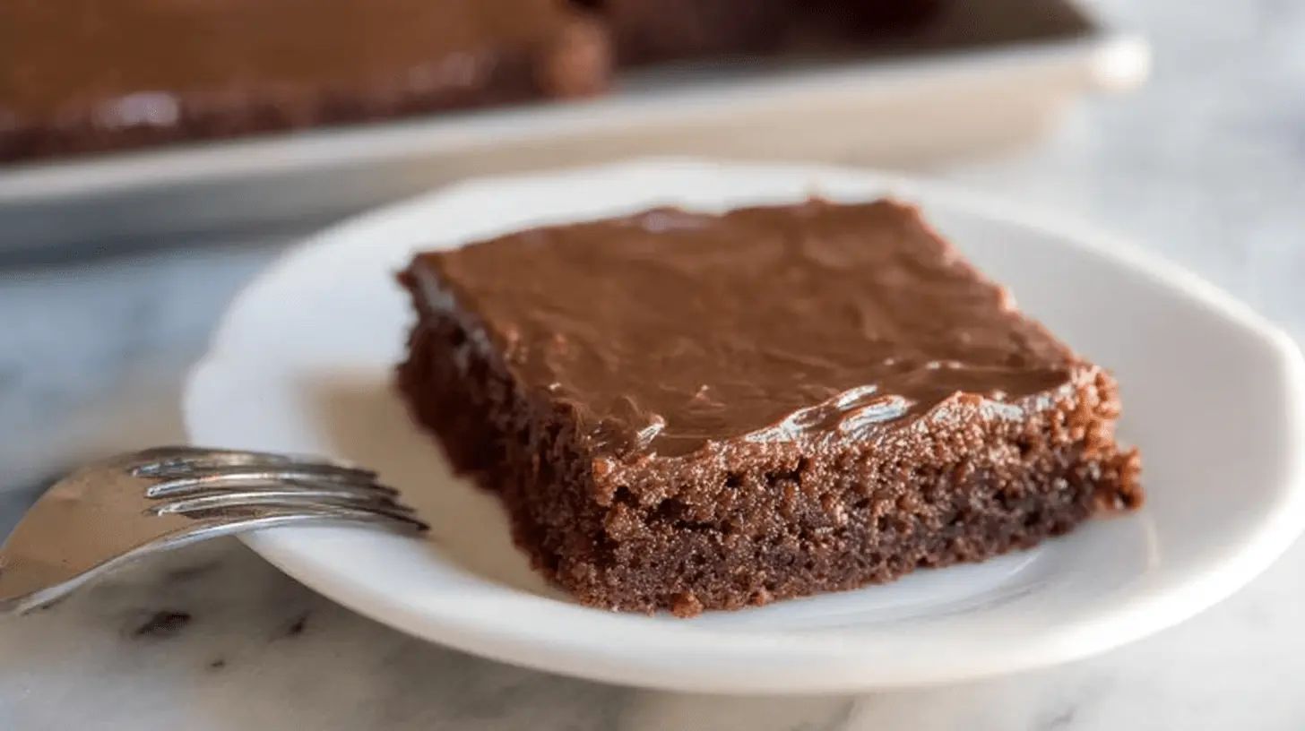 Delicious slice of chocolate Texas sheet cake with fudge frosting on a white plate.