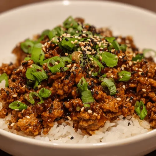 Appetizing bowl featuring savory ground chicken over fluffy white rice, garnished with fresh scallions and sesame seeds.