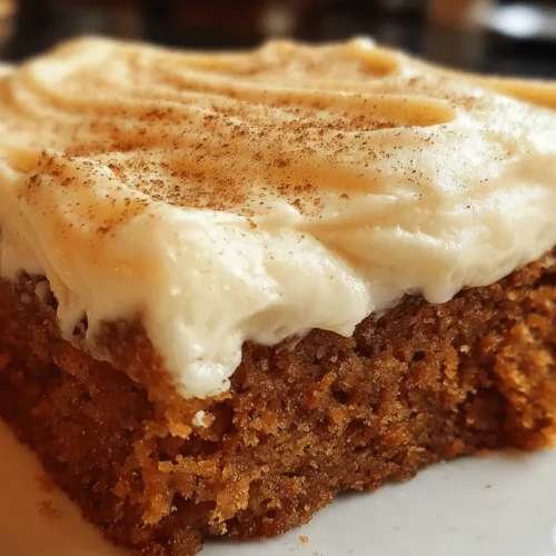 Close-up of a moist slice of spice cake with creamy white frosting, dusted with spice, on a white plate.