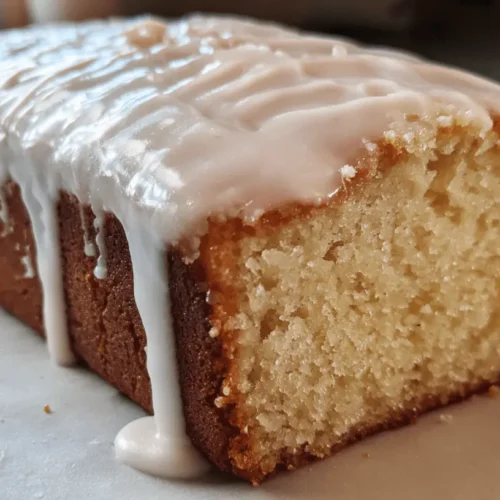 Freshly baked loaf cake generously drizzled with white glaze on a white surface.