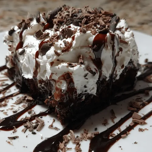 Decadent chocolate poke cake topped with whipped cream, chocolate syrup, and shavings on a white plate.