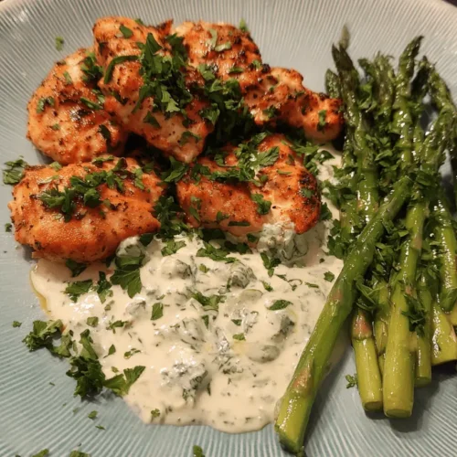 Beautifully plated keto chicken with creamy green sauce and fresh asparagus on a blue dish.